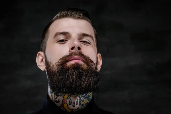 Крупный план портрета выразительного бородатого мужчины с татуировками на шее, изолированного на тёмном фоне. Снимок студии — стоковое фото