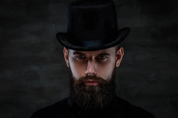 Un hombre barbudo serio y anticuado con un sombrero de copa, mirando a una cámara, aislado sobre un fondo oscuro . — Foto de Stock