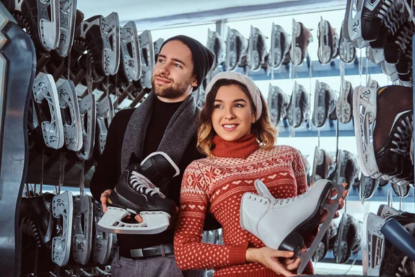Ungt par iført varmt tøj stående nær rack med mange par skøjter, vælge sin størrelse - Stock-foto