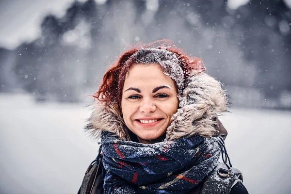 Porträt eines schönen rothaarigen Mädchens in warmer Kleidung mit Rucksack, das in der Nähe eines Winterwaldes steht — Stockfoto