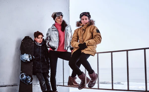 Familie dragen kleren poseren met snowboard naast een trapleuning op de besneeuwde strand — Stockfoto