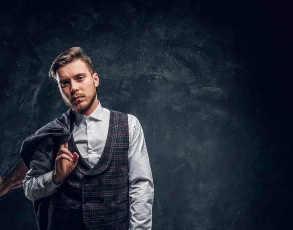 Elegant gekleideter Mann hält Jacke auf der Schulter, während er vor dunkel strukturierter Wand posiert — Stockfoto