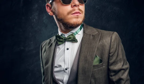 Ein stilvoller junger Mann mit Sonnenbrille im eleganten Anzug vor einer dunklen, strukturierten Wand — Stockfoto