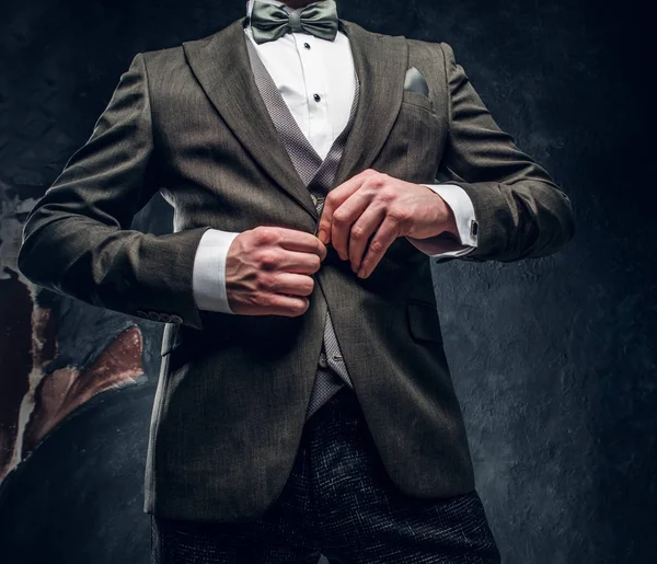 Un hombre elegante abotonando su elegante chaqueta contra una pared de textura oscura — Foto de Stock