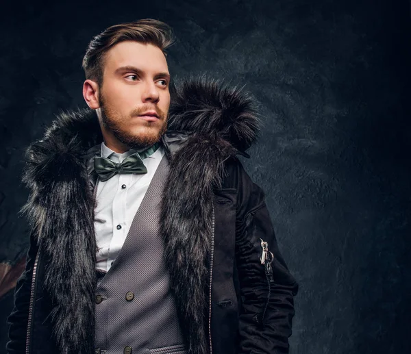 Retrato de un hombre vestido con un elegante traje y abrigo con una capucha de piel contra una pared de textura oscura — Foto de Stock