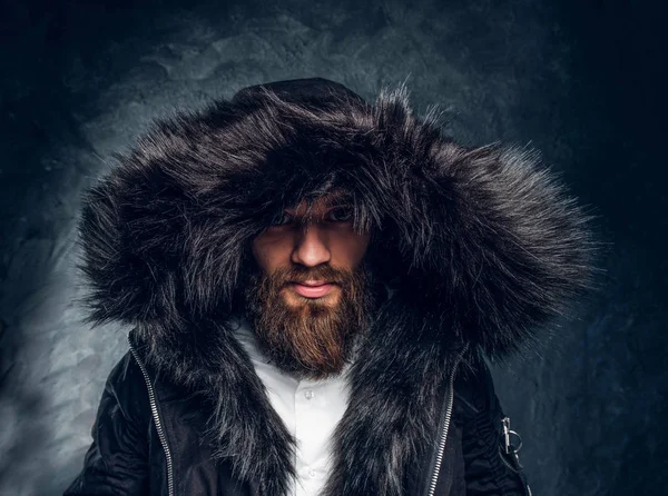 Портрет бородатого мужчины в пальто с меховым капюшоном на тёмной текстурной стене — стоковое фото