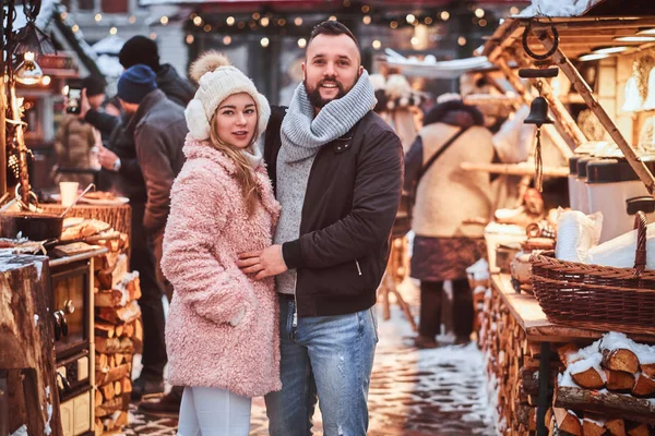 Casal atraente vestindo roupas quentes de pé juntos perto de um balcão de loja de uma feira de inverno em um tempo de Natal . — Fotografia de Stock