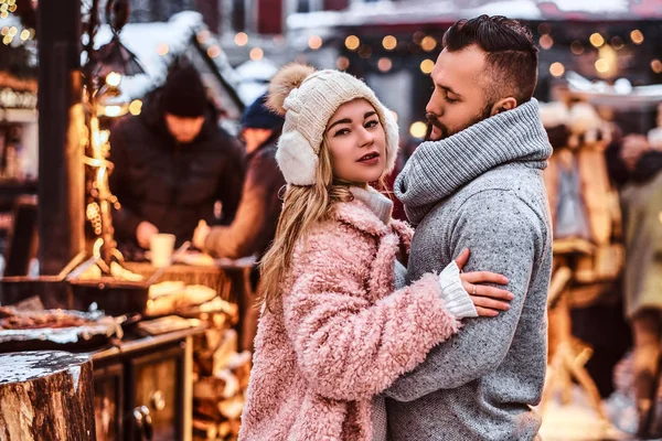 Un hombre guapo y encantadora chica abrazándose y disfrutando pasar tiempo juntos mientras están de pie en la feria de invierno en un tiempo de Navidad — Foto de Stock