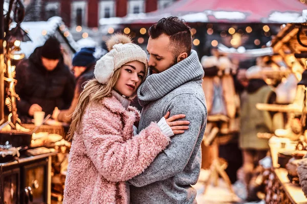 Un hombre guapo y encantadora chica abrazándose y disfrutando pasar tiempo juntos mientras están de pie en la feria de invierno en un tiempo de Navidad — Foto de Stock