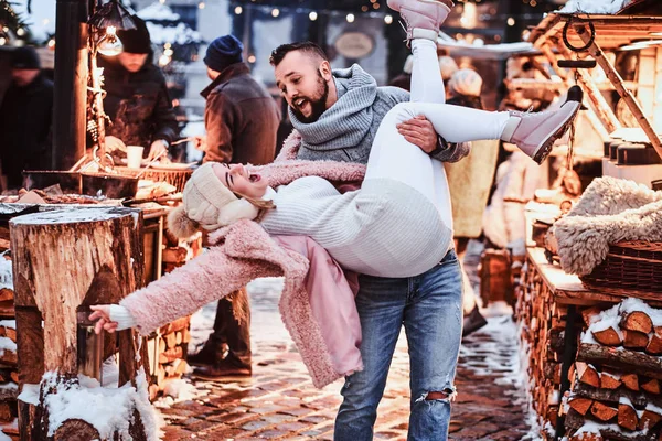 Um casal atraente apaixonado. Um homem bonito segurando sua namorada em mãos, se divertindo juntos enquanto estava na feira de Natal — Fotografia de Stock