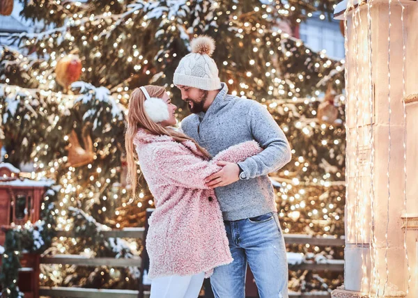 一对幸福的年轻夫妇穿着温暖的衣服, 拥抱并享受在城市圣诞树附近的时光. — 图库照片