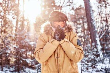 Sıcak giysiler ve gözlük, giymiş genç snowboard ısıtan ellerini karlı ormanda ayakta