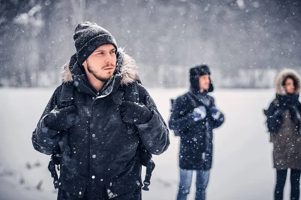 Ein junger Wanderer mit Rucksack, der mit seinen Freunden durch den winterlichen Wald wandert — Stockfoto