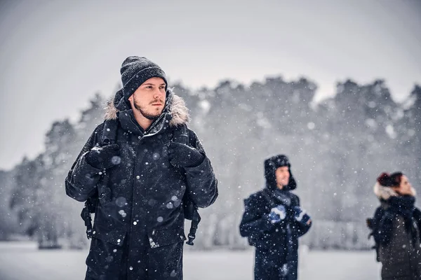 Egy fiatal turista fickó egy hátizsák, séta a téli erdőben a barátaival — Stock Fotó