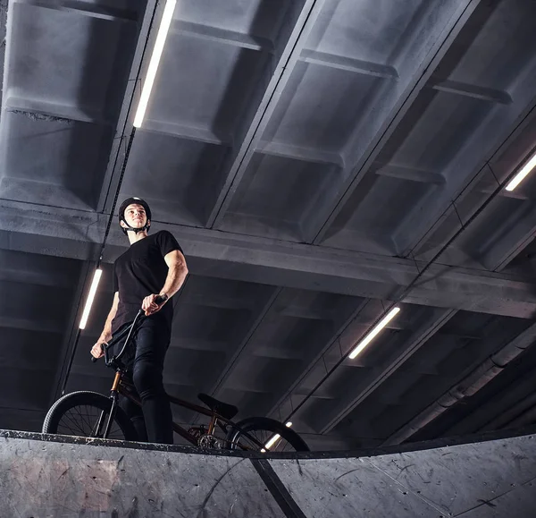 Joven con BMX preparándose para saltar en un parque de skate en el interior — Foto de Stock