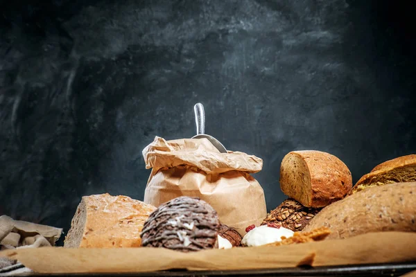 Baguette di pane fresco e muffin su un tavolo di legno su una parete strutturata scura . — Foto Stock