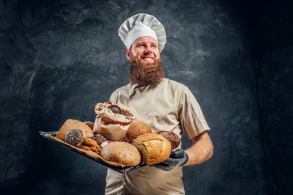 Um padeiro vestindo uma bandeja uniforme com produtos acabados de preparar de sua padaria — Fotografia de Stock