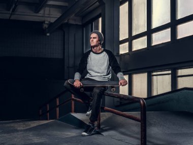 Gömlek ve holding onun yönetim kurulu skatepark kapalı bir eziyet demiryolu üzerinde otururken şapka giyen genç yakışıklı adam