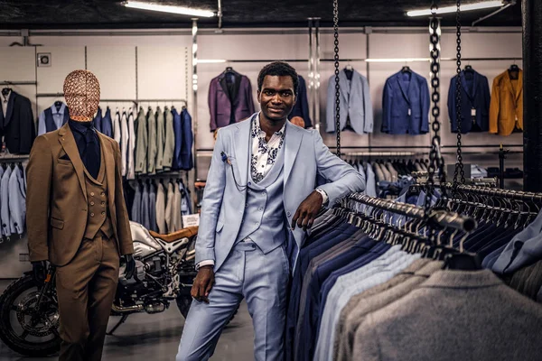 Elegantemente vestito uomo afro-americano appoggiato su un manichino in un negozio di abbigliamento maschile classico . — Foto Stock