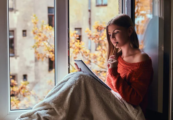 暖かいセーターの女の子が毛布で彼女の足をカバー、ノートは、開いているウィンドウの横にある窓の下枠の上に座って彼女のノート — ストック写真
