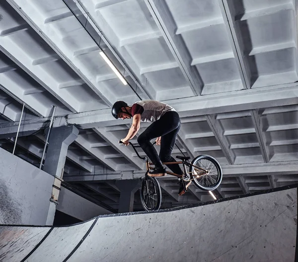 Молодой человек с BMX выполняет трюки в скейтпарке в помещении — стоковое фото