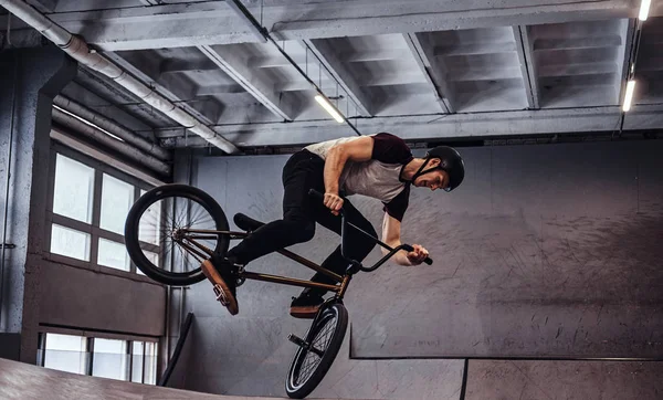 Молодой человек с BMX выполняет трюки в скейтпарке в помещении — стоковое фото