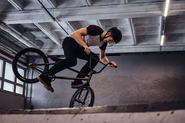 Молодий чоловік з BMX виконує трюки в скейтпарку в приміщенні — стокове фото