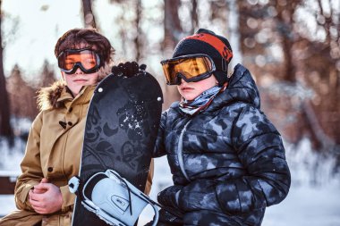 Bir snowboard bir parkta bir bankta oturmuş sıcak elbise giymiş iki genç kardeş