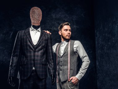 Karanlık terzi Studio özel özel yapılmış mens kıyafetli bir manken yanında poz kendine güvenen genç moda tasarımcısı 
