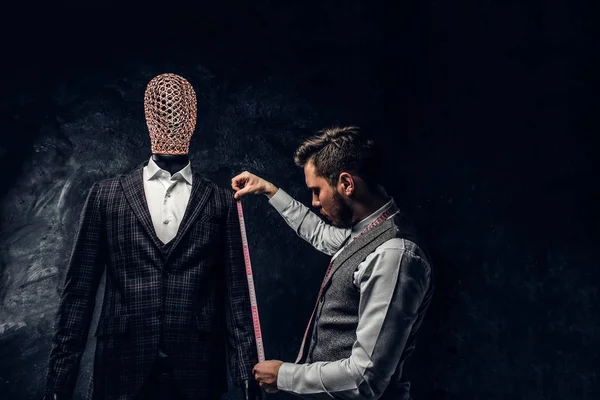 A fashion designer with a measuring tape check the length of the sleeves of a custom made elegant mens suit in a dark tailor studio — Stock Photo, Image