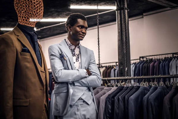 Uomo afro-americano vestito di blu elegante vestito in posa con le braccia incrociate in un classico negozio di abbigliamento maschile . — Foto Stock