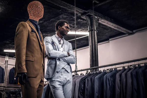 Homem afro-americano vestido de azul terno elegante posando com braços cruzados em uma loja de moda masculina clássica . — Fotografia de Stock