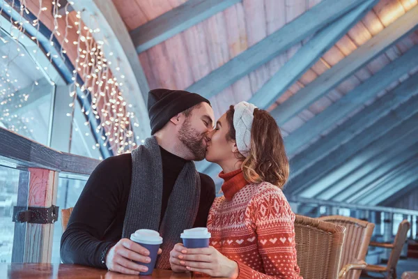 Jovem casal atraente em um encontro em uma pista de patinação no gelo, sentado à mesa no salão e bebendo café — Fotografia de Stock
