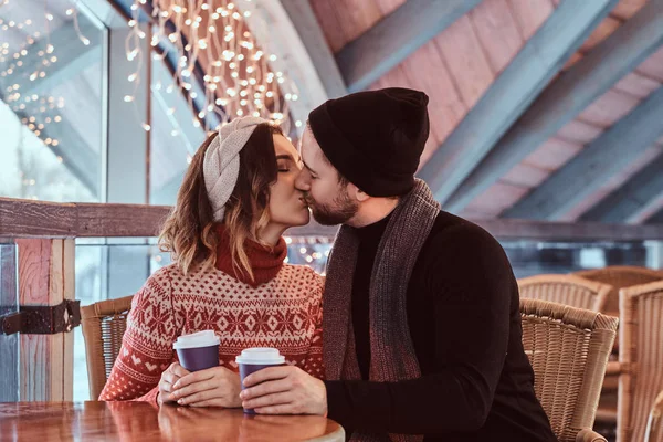 Jovem casal atraente em um encontro em uma pista de patinação no gelo, sentado à mesa no salão e bebendo café — Fotografia de Stock