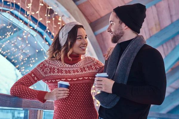 Joven pareja feliz en una cita en una pista de patinaje sobre hielo, de pie en el pasillo y beber café — Foto de Stock