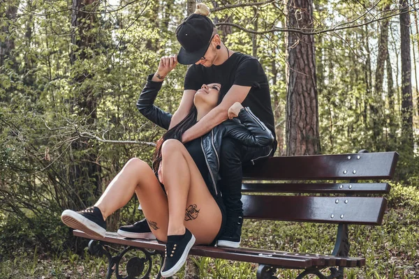 Пара влюбленных обнимается сидя на скамейке, наслаждаясь вместе в красивом летнем парке — стоковое фото