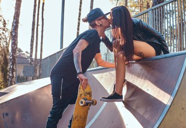 Şık çift aşık. Güzel kız bir rampa üzerinde oturan ve onun erkek arkadaşı skatepark yaz öpüşme.