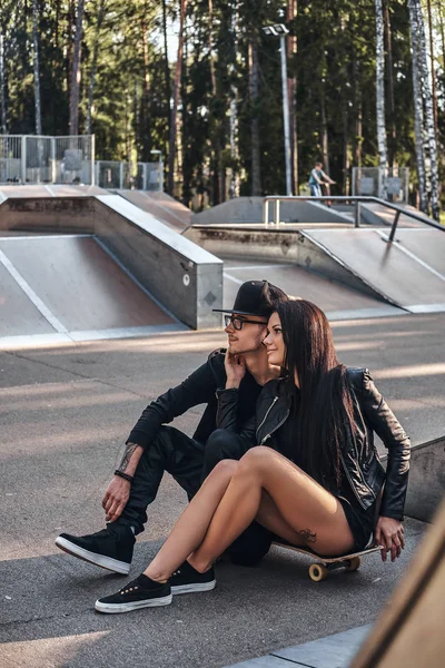 Couple in love together sits on a skateboard in a skate park at the summertime — Stock Photo, Image