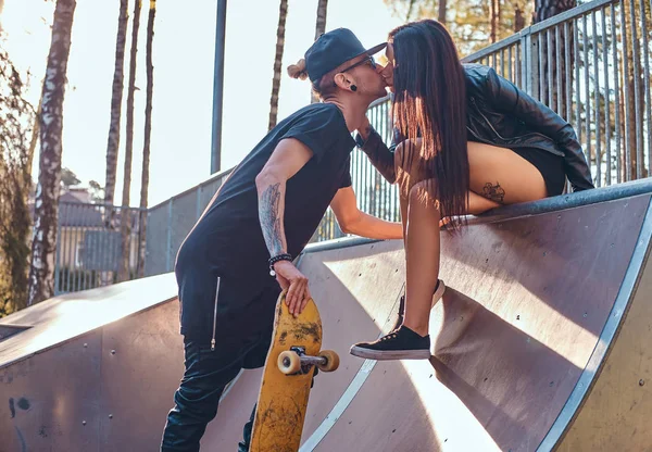 Couple élégant amoureux. Belle fille assise sur une rampe et embrassant son petit ami dans le skatepark en été — Photo