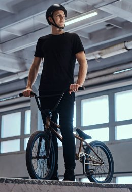 Bir skatepark kapalı onun bisiklet ayakta olan koruyucu kask içinde genç bir adam portresi