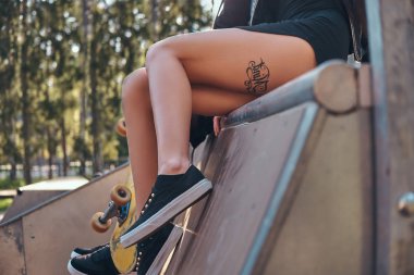 Dövmeli kızlar bacaklar. Yaz aylarında bir rampa skate park üzerinde oturan genç şık kız.