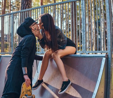 Şık çift aşık. Güzel kız bir rampa üzerinde oturan ve onun erkek arkadaşı skatepark yaz öpüşme.
