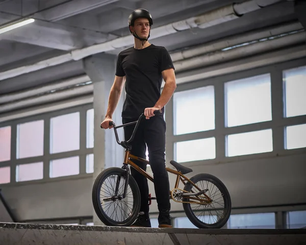 Портрет молодого чоловіка в захисному шоломі з велосипедом, що стоїть в скейтпарку в приміщенні — стокове фото