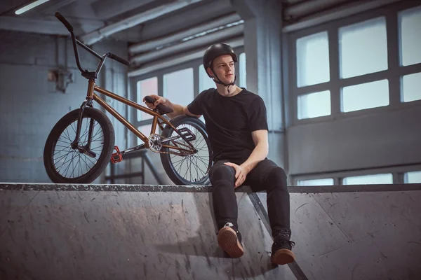 Bmx 라이더는 skatepark 실내에 그의 자전거 트릭 연습 후 휴식 — 스톡 사진