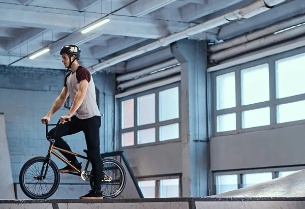 Молодой человек с BMX готовится прыгнуть в скейтпарк в помещении — стоковое фото