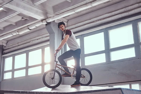 Retrato de un joven en casco protector con su bicicleta de pie en un parque de skate en el interior —  Fotos de Stock