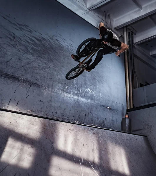 Jovem BMX fazendo truques loucos em sua bicicleta no skatepark dentro de casa . — Fotografia de Stock