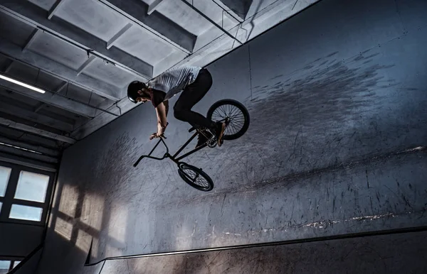 Молодий чоловік з BMX виконує трюки в скейтпарку в приміщенні — стокове фото
