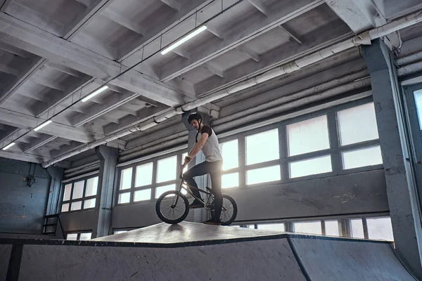 Joven con BMX preparándose para saltar en un parque de skate en el interior — Foto de Stock