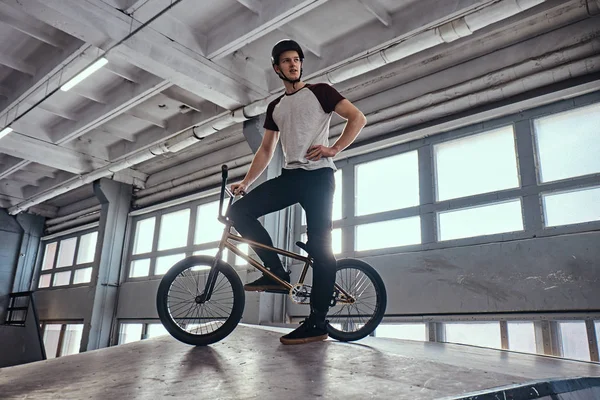 BMX jinete de pie con su bicicleta preparándose para saltar en un parque de skate en interiores — Foto de Stock